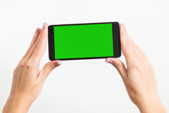 Close up mockup image of woman's two hands holding black mobile phone with blank green screen isolated on white background. Horizontal color photography.