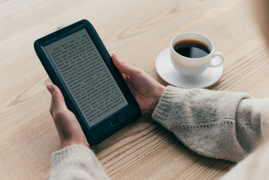 cropped view of woman studying with e-book near cup of coffee
