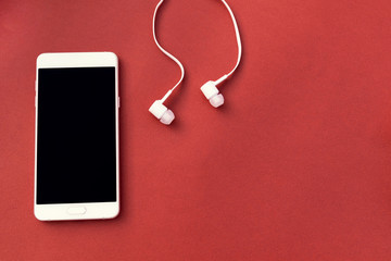 White smartphone and white headphones on red background. Place for text.