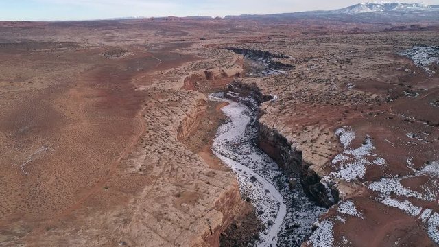 Aerial view flying down into canyon from above the desert in Utah moving down to the rim viewing snow in the canyon near Moab.