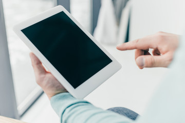 cropped view of man pointing with finger at digital tablet with blank screen in hands