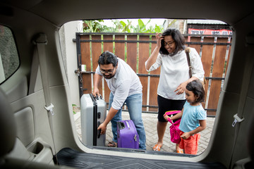 portrait of asian family with kid put a suitcase in to the car trunk, ready for holiday together