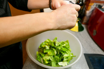 Close up of female hands and woman preparing green salad, cooking in kitchen. Housewife slicing and prepared fresh salad. Chef cutting greens in plastic bowl. Vegetarian and healthy cooking concept.