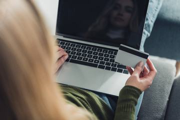 selective focus of woman using laptop with blank screen while holding credit card