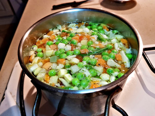 Boiling vegetable soup of peas, carrots and celery is cooked in a saucepan on a home gas stove