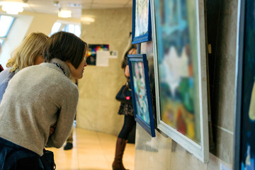rear view of younga caucasian woman stading in an art gallery in front of two large colorful paintings - obrazy, fototapety, plakaty