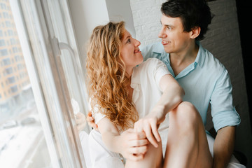 Happy girl and man hugging near window in home. 