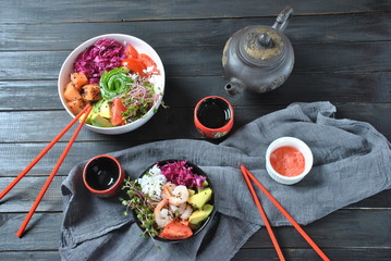 Organic food. Fresh seafood recipe. Two fresh poke bowls with salmon, shrimps, rice, red cabbage, avocado, cherry tomatoes and radish sprouts on wooden background. Food concept Poke Bowl