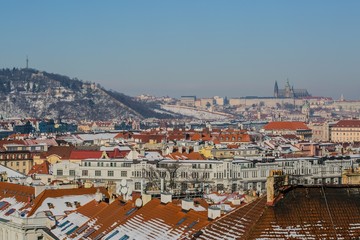 Prague, Czech Republic / Europe - February 5 2019: Scenic view of Prague city, Prague castle and Petrin tower from Vysehrad overlooking red roofs covered with snow, sunny day, clear blue sky