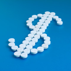 White pills spilling forming a dollar sign on a blue background. Isolated