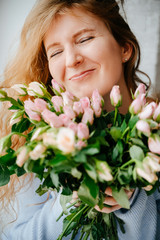 Portrait of a young beautiful girl with a bouquet of roses near window. Curly flowing red hair.