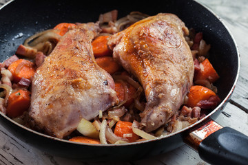 Fried rabbit legs on frying pan with vegetables