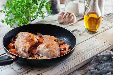 Fried rabbit legs on frying pan with vegetables