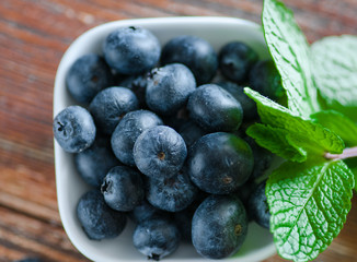 blueberries on a table in a white saucer and in an old cup