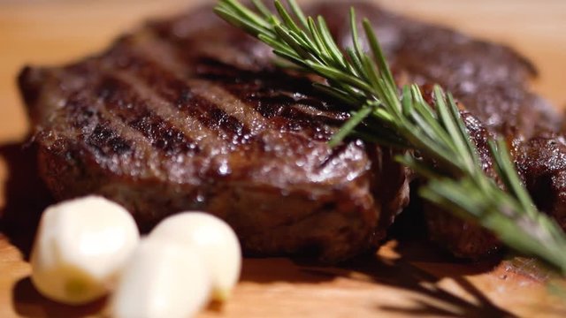 Delicious grilled steak lying on the cutting board with garlic close up. Fresh rosemary fall on the meat