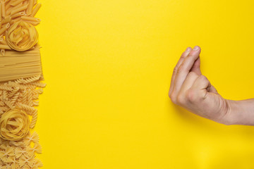 man shows a traditional Italian gesture on a yellow background with different kinds of pasta