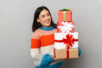 Photo of surprised woman 30s holding bunch of gift boxes while standing, isolated over gray...