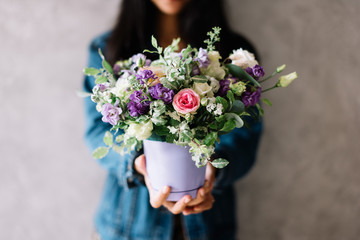 Very nice young woman holding beautiful blossoming bouquet of fresh mattiola, roses, eustoma, carnations flowers in the flower pot on the grey wall background 