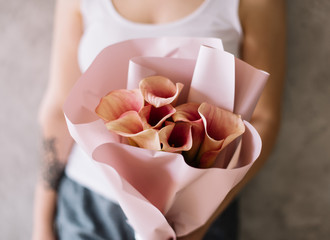 Very nice young woman holding beautiful blossoming pink calla lily bouquet oon the grey wall background 