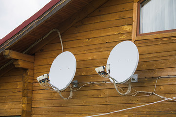 Two satellite dishes attached to wooden wall of countryside house. Horizontal color photography.