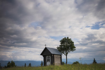 Obraz premium Old weathered small wooden chapel isolated in beautiful countryside landscape. Horizontal color photography.
