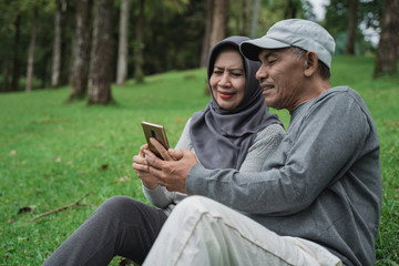 happy senior muslim couple using smartphone together in the park. old people with modern technology