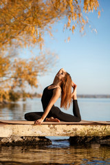 Young woman practicing yoga exercise at quiet pier in autumn park