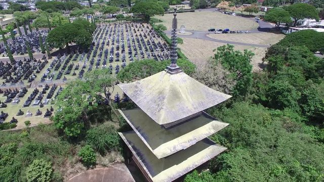 Aerial drone 360 panorama circling a pagoda in Honolulu, Hawaii with a cemetery and tall buildings in the background.