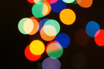 Multi-color holiday garland. Garland is blurred. Many colorful round lights. Fully defocused photo. Blurred background and foreground. Holiday mood. New Year and Christmas is coming.