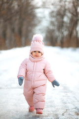 A beautiful young girl wearing a pink jumpsuit running in a snowy winter park.