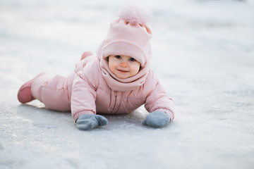 A beautiful young girl wearing a pink jumpsuit, lying on the snow in a snowy winter park
