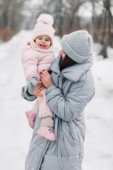 Beautiful young girl in a pink jumpsuit playing with her mother in a snowy winter park.