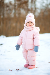 Little beautiful girl in pink jumpsuit in a snowy winter park