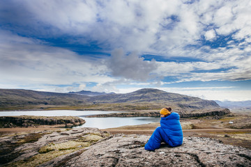 Young woman in warm blue sleeping bag ,  on the stones with northern mass, Iceland