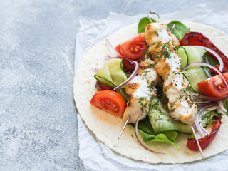 Grilled chicken on metal skewers with Greek sauce and fresh vegetables on the pita. Greek cuisine. Copy space