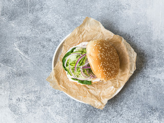 Homemade fish burger of white fish fillet with cucumber slice, red onion, fresh dill and spinach on a white plate