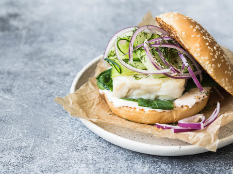 Homemade Fish Burger Of White Fish Fillet With Cucumber Slice, Red Onion, Fresh Dill And Spinach On A White Plate