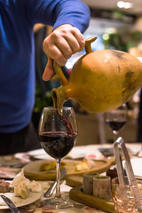 A man pours red traditional wine from a clay jug into a glass in a restaurant