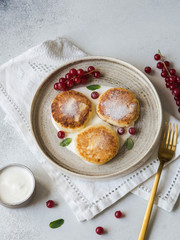 Homemade cheese cakes from cottage cheese served on a white ceramic plate with mint, sour cream and red currant on a grey background. Top view