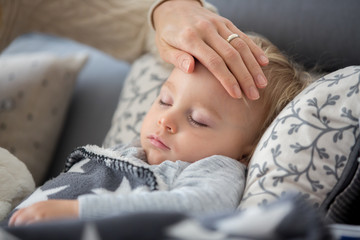 Sick child, toddler boy lying in bed with a fever, resting at home