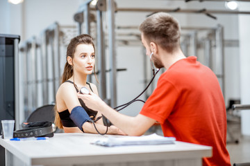 Obraz premium Man as a rehab in red uniform measuring pressure to a young woman sitting at the rehabilitation gym