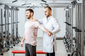 Professional senior physiotherapist doing manual treatment to a man standing in the rehabilitation gym