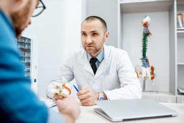 Portrait of a senior therapist during the medical consultation showing anatomical model of vertebras in the office