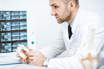 Therapist holding anatomical model of vertebras with intervertebral hernia during the medical...