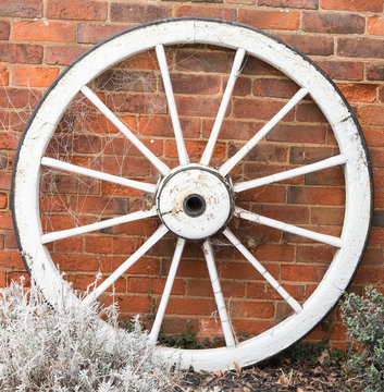 Vintage wooden cart wheel leaning against a brick wall