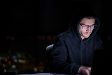 hacker using laptop computer while working in dark office