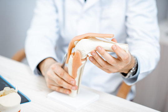 Close-up of the therapist showing knee joint model during the medical consultation