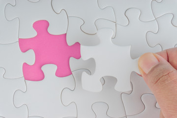 Fototapeta premium Hand put the last piece of jigsaw puzzle closeup to complete the mission. Selective focus and crop fragment