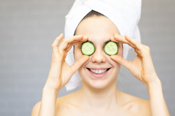 Young beautiful girl smiling hiding eyes behind cucumber slices over white background. Beauty skincare and cosmetology	