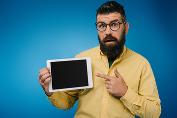 interested bearded man pointing at digital tablet with blank screen, isolated on blue